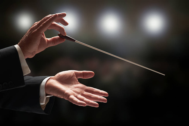Dirigent dirigiert ein Orchester mit Publikum im Hintergrund - Foto, Bild
