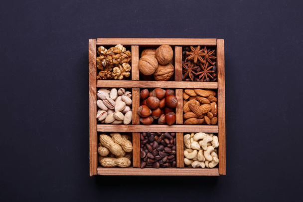 Assortment of nuts in a wooden box on a black background - healthy snack. Top view. Copy space - Фото, изображение