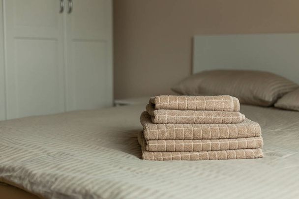 Stack of beige hotel towel on bed in bedroom interior. Soft focus. - Foto, immagini