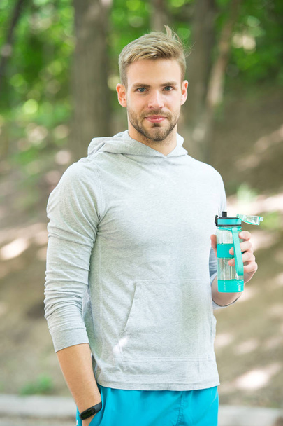 Refreshing vitamin drink after outdoor workout. Man athletic appearance holds water bottle. Guy athlete hold bottle care hydration body after workout. Athlete drink water after training in park - Zdjęcie, obraz