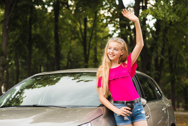 Menina sorrir e cumprimentar com a mão perto do carro
 - Foto, Imagem