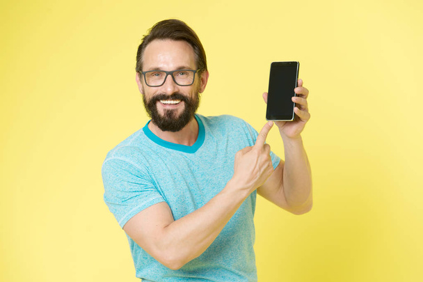 Man excited about new mobile opportunities. Guy eyeglasses cheerful pointing at smartphone. Man happy user interact application for smartphone. Guy bearded interact mobile interface application - Foto, imagen