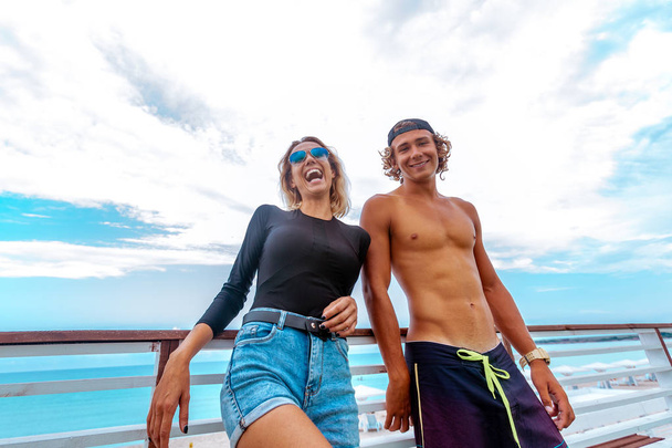 Усміхнені молоді активні пари серферів розважаються на пляжі після спорту. Красивий морський пейзаж на фоні
 - Фото, зображення