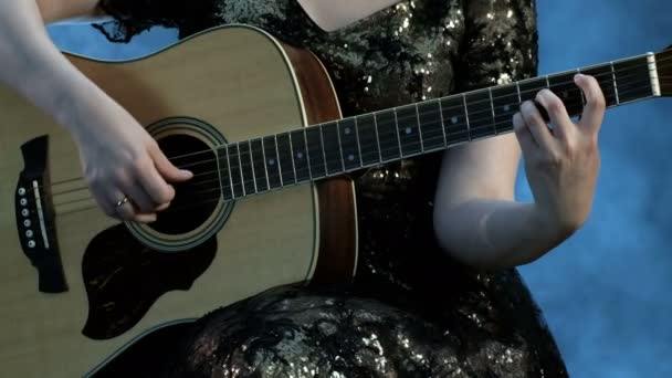 Ein Mädchen im Abendkleid spielt eine sechssaitige Akustikgitarre. die rechte Hand berührt die Saiten, die linke hält die Akkorde auf dem Griffbrett. Rauch im Hintergrund. Tag der Musik. - Filmmaterial, Video