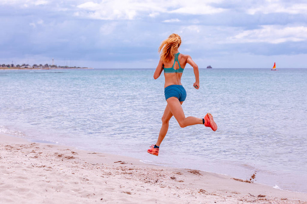 Спортивная женщина бегает по красивому песчаному пляжу, ведет здоровый образ жизни, наслаждается активным летним отдыхом у моря
 - Фото, изображение