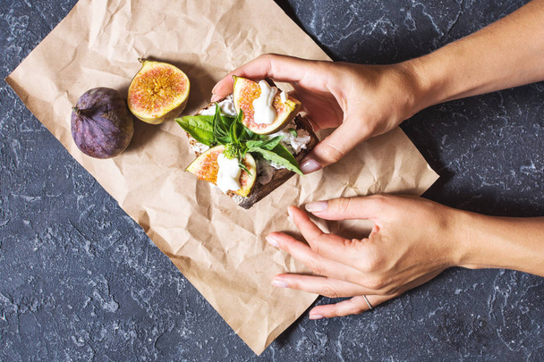 Frauenhände halten Feigen-Frucht-Sandwich auf schwarzem Steinhintergrund - Foto, Bild