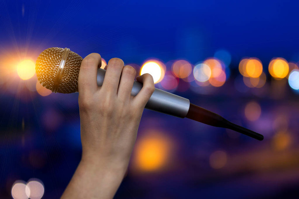 Микрофон в женских руках крупным планом на абстрактном боке фоне. Размытый фон с огнями
 - Фото, изображение