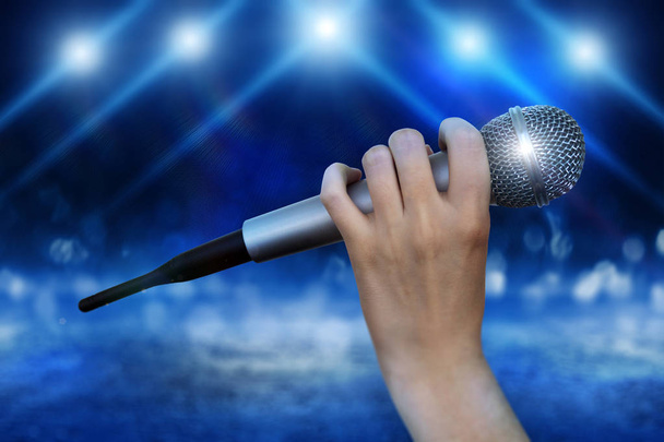 Микрофон в женских руках крупным планом на абстрактном боке фоне. Размытый фон с огнями
 - Фото, изображение