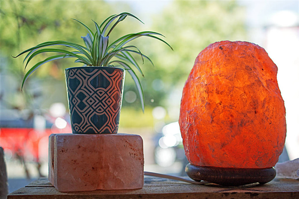 Растение и соляная лампа на деревянной коробке перед оконным макро крупным планом
 - Фото, изображение