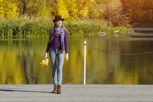 Młoda kobieta w kapeluszu stoi na molo. Jesienny dzień słoneczny. Widok z tyłu - Zdjęcie, obraz