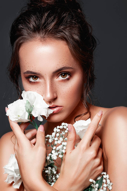 Glamour portrait of beautiful woman model with fresh daily makeup and romantic wavy hairstyle.  Fashion shiny highlighter on skin, sexy gloss lips make-up and dark eyebrows. Cute freckles on young face. Sensual woman with white flowers. - Photo, Image
