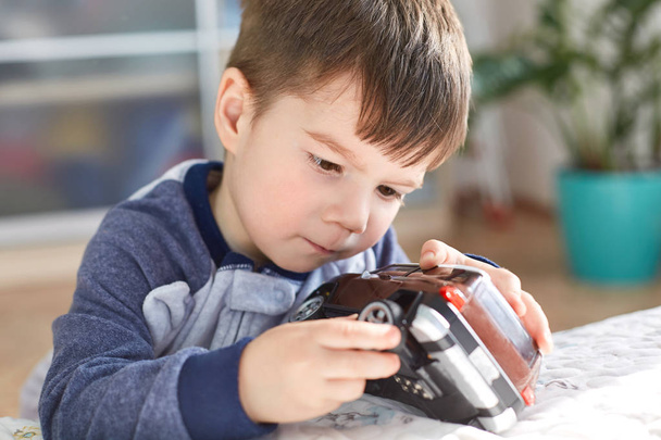 Close up shot of attractive brunet male kid plays with his favourite toy car, tries to repair wheel, has concentrated look, spends free time at home, doesn`t go to kindergarten. Children and leisure - Photo, Image