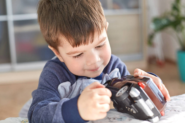 Indoor shot of good looking small kid holds toy car in hands, poses indoor against cozy domestic interior, likes to play with toys, has appealing look. alegre lindo chico preescolar siendo travieso
 - Foto, imagen