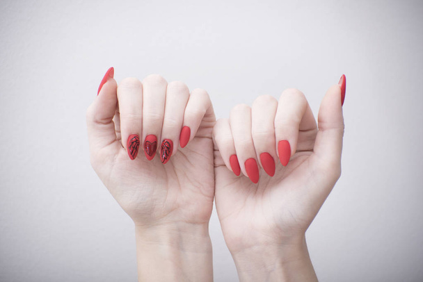 Punainen manikyyri, jossa on kuvio. Naisen kädet valkoisella taustalla
 - Valokuva, kuva