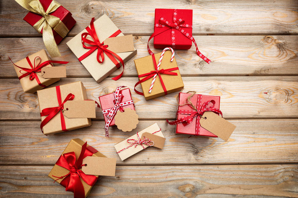 Caixas de presente de Natal com fitas vermelhas e etiquetas em branco no fundo de madeira, espaço de cópia, vista superior
 - Foto, Imagem