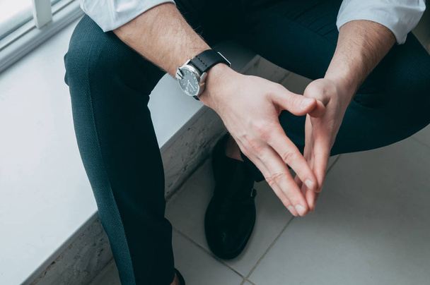 abgeschnittene Ansicht des Chefs, der die Hände zusammenhält, auf seinem Arm eine teure und stylische Uhr, auf dem Hintergrund des Beines die Ansicht von oben - Foto, Bild