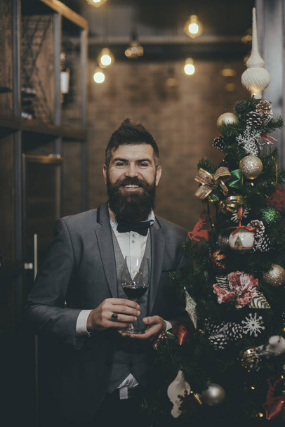 Christmas, man with beard in restaurant. New year man at xmas party celebration. Hipster at Christmas tree with wine glass. Drink alcohol on winter holiday. Thanksgiving Day toast greeting of guy. - Photo, Image