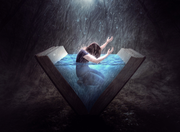 Una mujer levanta sus brazos en alabanza mientras está en un libro lleno de agua
. - Foto, imagen
