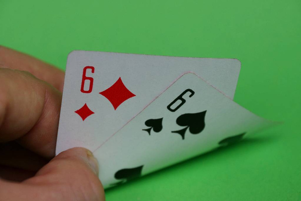 Zwei Spielkarten mit ein Paar Sechsen in Finger der Hände am grünen Tisch - Foto, Bild