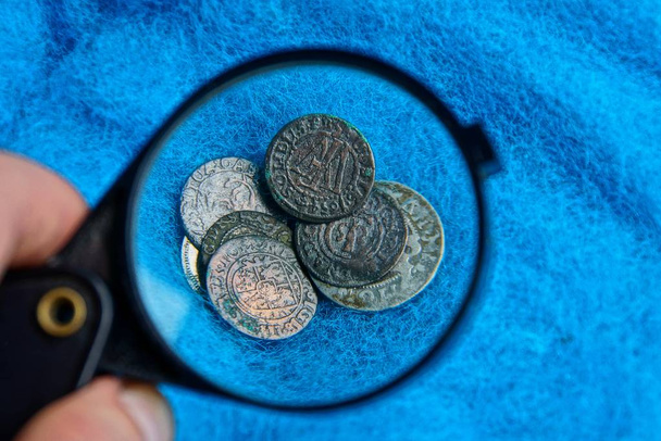 青いウール織物に虫眼鏡の下杭に古い銀と銅のコイン - 写真・画像