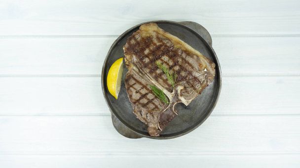 gegrilltes T-Bone Beef Steak auf weißem Holzboden Hintergrund Requisiten Dekoration Zitrone, Draufsicht mit Kopierraum für Ihren Text - Foto, Bild