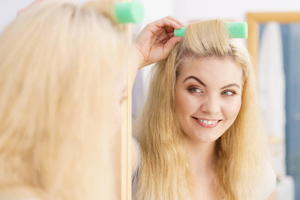 Blonde woman using hair rollers to create beautiful hairstyle on her hairdo. - Foto, Bild