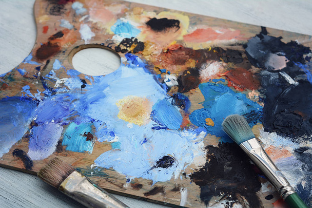 Artist's palette with colorful oil paint strokes and paintbrushes on white wooden background. Art concept - Fotoğraf, Görsel