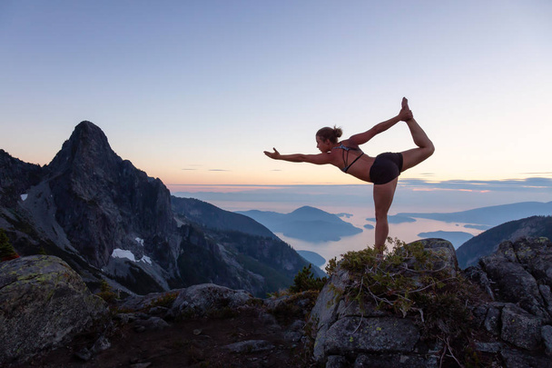 Girl practicing yoga on top of a mountain during a vibrant summer sunset. Taken in Howe Sound, near Vancouver, BC, Canada. - Photo, image