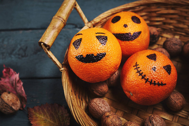 Halloween painted oranges with faces in a wicker basket on a wooden background - Φωτογραφία, εικόνα