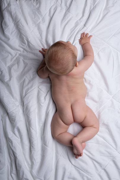 Маленький новорожденный ребенок пытается ползти на белых постельных принадлежностях просматривается сверху показывая свои милые маленькие ягодицы
 - Фото, изображение
