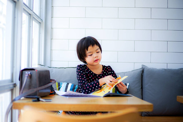 Asijská holčička hraje stricker knihu v restauraci, s dlaždici bílé zdi v pozadí - Fotografie, Obrázek
