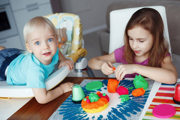 İki mutlu çocuk sarışın erkek ve kız evde masada oturma oynamak - Fotoğraf, Görsel