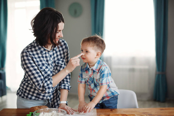 Mère et fils vêtus de chemises à carreaux sont cuits dans la cuisine de farine et de pâte
 - Photo, image