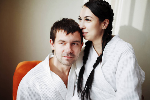 Young husband and wife of white coats play and smile in an orange armchair in a hotel room. Close up. - Foto, Bild