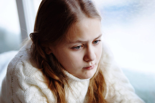 Joven linda chica adolescente emocional con trenzas se encuentra junto a la ventana interior. Lectura y sonrisa
 - Foto, imagen