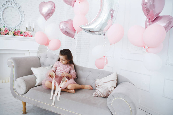 Νέοι μπαλαρίνα σε ένα ροζ φόρεμα κάθεται σε ένα γκρι καναπέ με pointes στα χέρια - Φωτογραφία, εικόνα