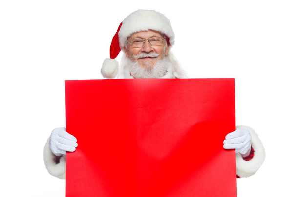 Рождество. Санта-Клаус в белых перчатках держит пустой картон красного цвета. Место для рекламы, для текста, пустого пространства. Скопировать-вставить. Изолированный на белом фоне
. - Фото, изображение
