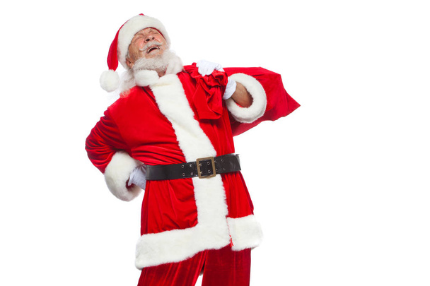 Navidad. Santa Claus está sufriendo de dolor de espalda y sostiene una bolsa roja con regalos en la espalda. Aislado sobre fondo blanco
. - Foto, imagen