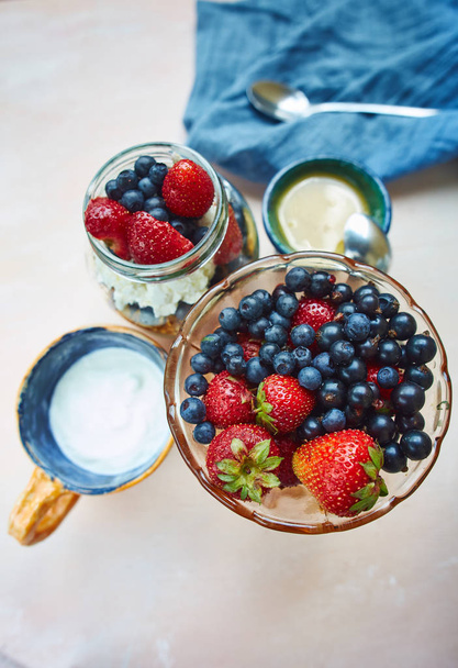 set for summer breakfast. top view of vase with fresh berries, bank with berries, cottage cheese and granola, honey and sour cream on pink wooden table - Fotó, kép