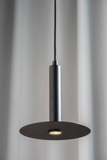 Black metallic lamp hanging on gray curtain background - Foto, Imagen