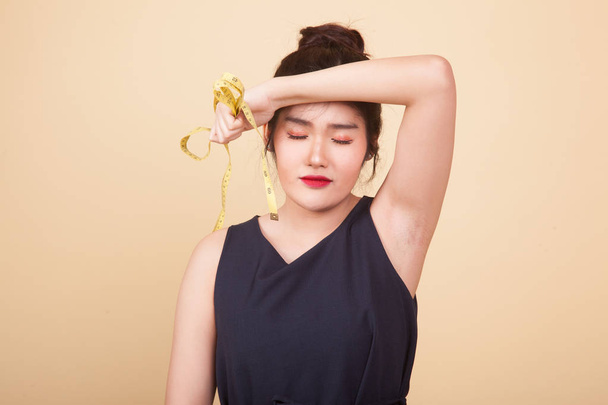 Unhappy young Asian woman with measuring tape  on beige background - Foto, afbeelding