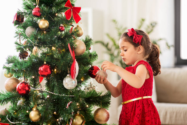 little girl decorating christmas tree at home - Fotó, kép
