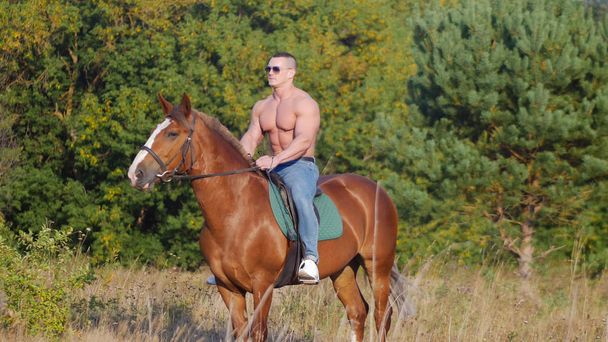Brutális erős fiatalember lovagol egy lovat a területen nyáron - Fotó, kép