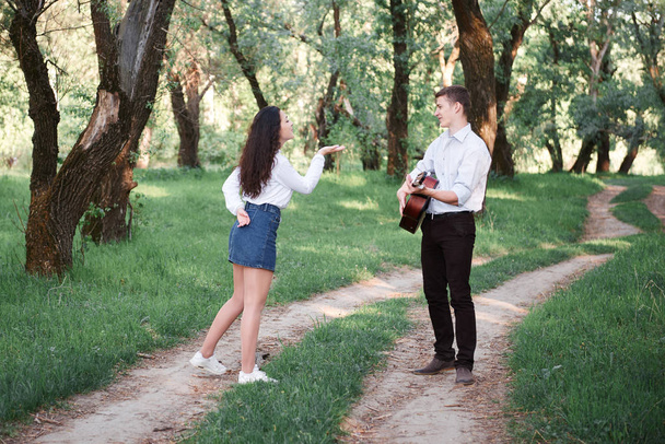 νεαρό ζευγάρι περπάτημα στο δάσος και να παίζει κιθάρα, καλοκαίρι φύση, έντονο ηλιακό φως, σκιές και πράσινα φύλλα, ρομαντικά συναισθήματα - Φωτογραφία, εικόνα