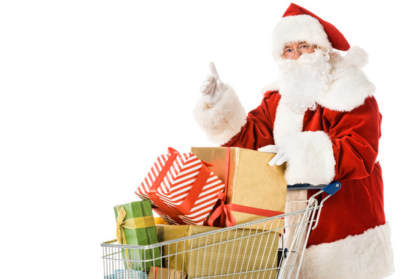 Weihnachtsmann mit Einkaufswagen voller Geschenkboxen, die isoliert auf weiß zeigen - Foto, Bild