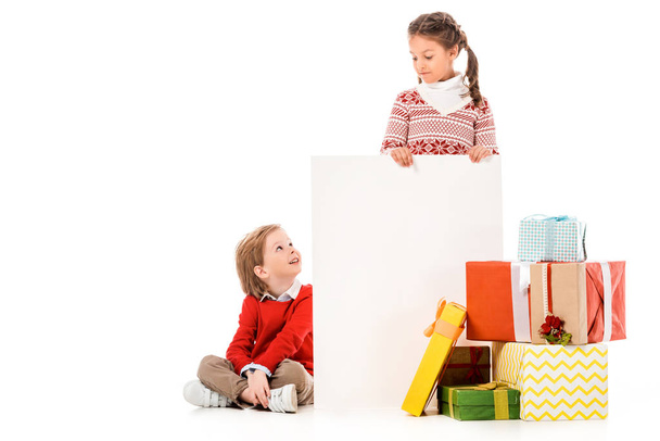 lindos niños pequeños con pila de regalos de Navidad y tablero en blanco aislado en blanco
 - Foto, Imagen
