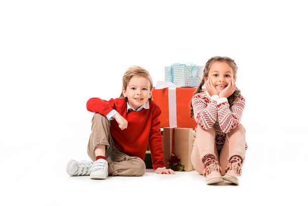 adorable little kids sitting on floor with pile of christmas gifts isolated on white - Fotó, kép