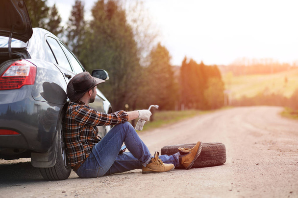 Man is sitting on the road by the car - Foto, imagen