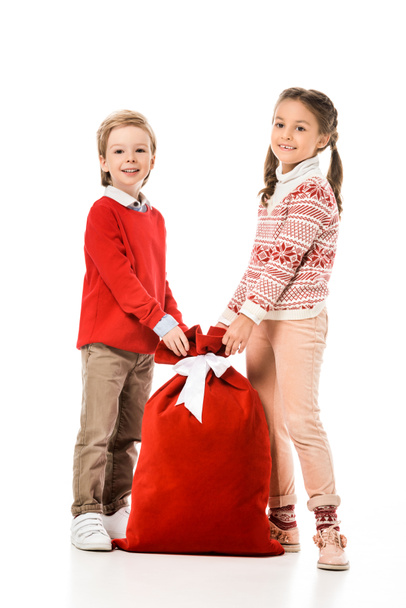 usmívající se malé děti s pytlem na dárky santa při pohledu na fotoaparát izolované na bílém - Fotografie, Obrázek