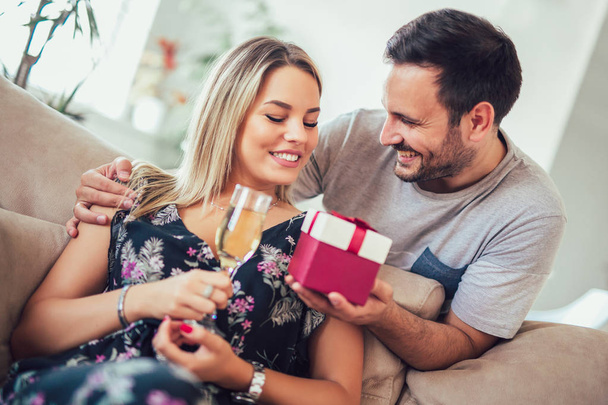Lächelnder junger Mann überrascht fröhliche Frau mit Geschenkbox zu Hause - Foto, Bild